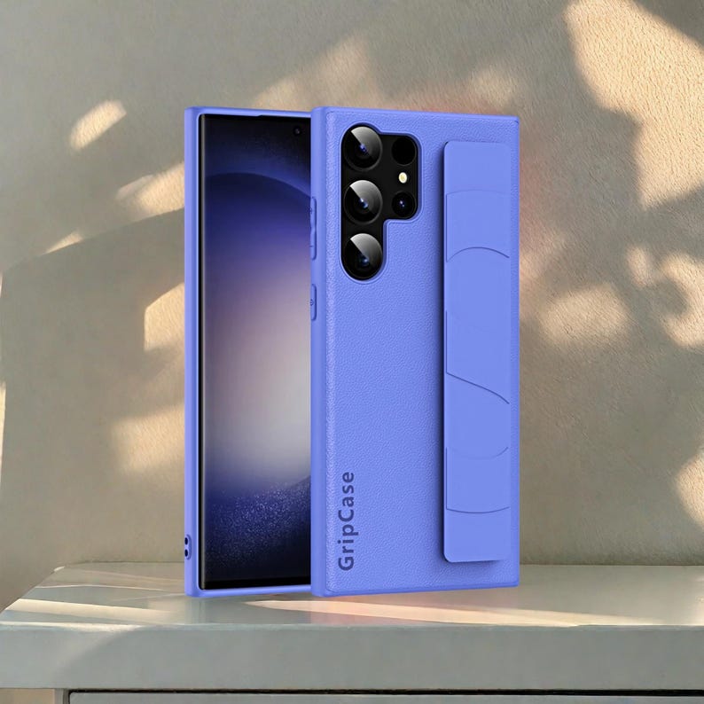 May include: A periwinkle blue phone case with a built-in grip and camera cutouts. The case is designed to fit a smartphone and has the text "GripCase" printed on the side. The phone's screen is visible.