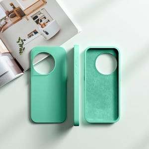 May include: Three mint-green phone cases are displayed on a white surface. One case is shown from the front, one from the side, and one from the inside. The cases have a smooth, matte finish and a circular cutout for the camera.