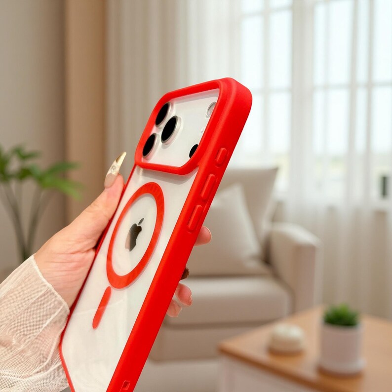 Puede incluir: Una funda transparente para tel&eacute;fono con borde rojo y dise&ntilde;o de c&iacute;rculo rojo. La funda presenta un logotipo de Apple negro y un recorte para la c&aacute;mara. La funda est&aacute; dise&ntilde;ada para proteger el tel&eacute;fono de ara&ntilde;azos e impactos.