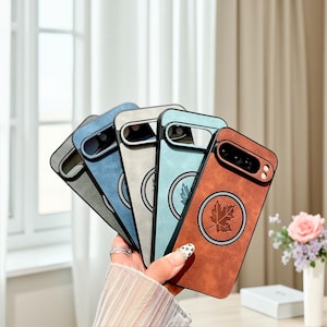 May include: A hand holds a collection of phone cases in various colors: gray, blue, and brown. Each case features a circular emblem with a leaf design. The cases have a textured, leather-like appearance.