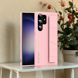 May include: A light pink phone case with a built-in grip and camera cutouts. The case is shown with a phone inside, and the text "GripCase" is printed vertically on the side. The phone screen displays a blue and white gradient.