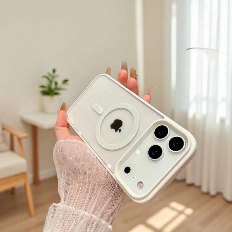 Puede incluir: Una funda de tel&eacute;fono transparente y blanca con un anillo de carga magn&eacute;tico blanco y un logotipo de Apple negro. La funda tiene un borde blanco alrededor de la c&aacute;mara y los bordes del tel&eacute;fono. Dise&ntilde;ado para un tel&eacute;fono inteligente.