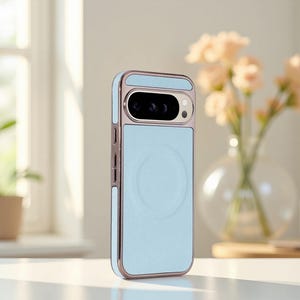 Può includere: Custodia per telefono azzurra con retro strutturato e cornice metallica color oro rosa. La custodia presenta un design circolare sul retro e un ritaglio per la fotocamera. La custodia è mostrata davanti a una finestra e un vaso di fiori.