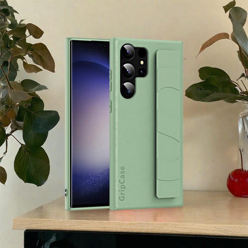May include: A light green phone case with a textured finish and a built-in grip. The case has a camera cutout and the text "GripCase" printed vertically. The phone screen is visible on the left side of the image.