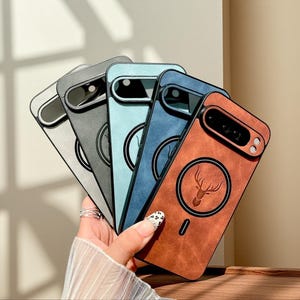 Puede incluir: Cinco fundas para teléfono en plata, gris, azul claro, azul oscuro y marrón. Cada funda presenta un diseño circular con la silueta de un ciervo y un recorte para la cámara.