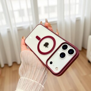 Puede incluir: Una funda transparente para tel&eacute;fono con un borde burdeos y un dise&ntilde;o circular burdeos. La funda tiene un interior blanco y un recorte para la c&aacute;mara del tel&eacute;fono.