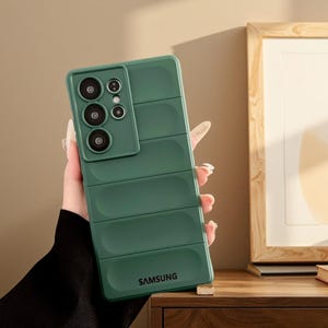 Peut inclure: Coque de téléphone vert foncé pour Samsung. Le boîtier présente un design texturé et nervuré et un module caméra avec plusieurs objectifs. Le logo Samsung est imprimé en bas.
