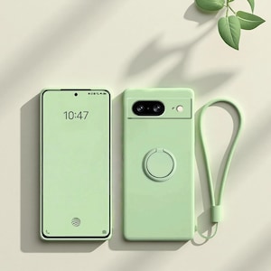 Puede incluir: Una funda de teléfono verde claro con un teléfono a juego y una correa para la muñeca. La funda del teléfono tiene un recorte para la cámara, un soporte para anillos y una correa para la muñeca. La pantalla del teléfono muestra la hora 10:47. El teléfono está al lado de la funda.