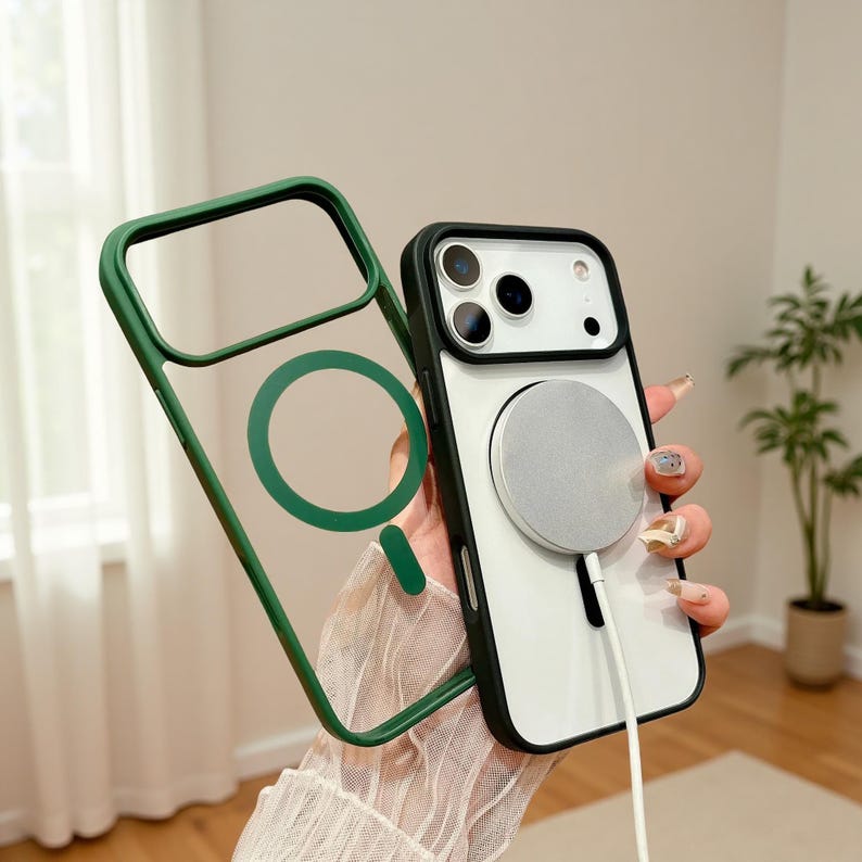 Puede incluir: Una funda transparente para tel&eacute;fono con borde verde y c&iacute;rculo verde a juego. La funda est&aacute; junto a un tel&eacute;fono blanco y negro con un cargador magn&eacute;tico plateado. El tel&eacute;fono est&aacute; en manos de una persona.