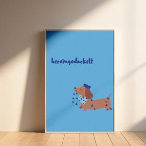K&ouml;nnte beinhalten: Ein gerahmtes Poster mit hellblauem Hintergrund zeigt einen Cartoon-Dackel mit blauer M&uuml;tze, der eine Schnur mit herzf&ouml;rmigen blauen Luftballons h&auml;lt. Der Text "hereingedackelt" ist in blauer Schrift oben geschrieben.