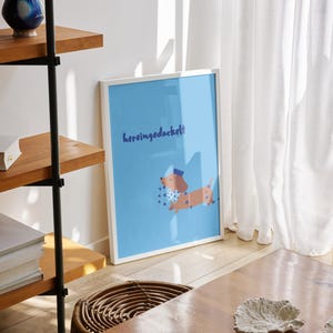 K&ouml;nnte beinhalten: Ein gerahmter Kunstdruck mit einer Dackel-Illustration auf hellblauem Hintergrund. Der Dackel tr&auml;gt einen Hut und einen gepunkteten Schal. Der Text "hereingedackelt" steht &uuml;ber dem Hund. Der Druck wird auf einem Holzboden pr&auml;sentiert.