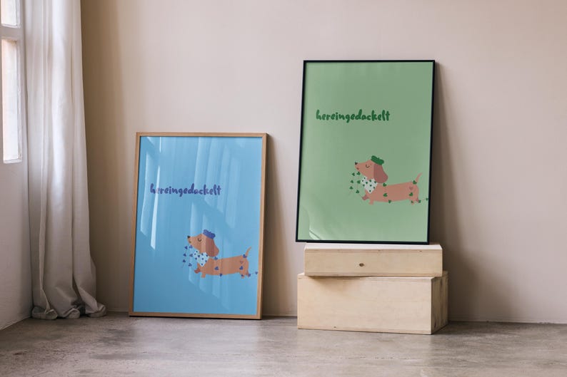 K&ouml;nnte beinhalten: Zwei gerahmte Kunstdrucke mit einer Cartoon-Dackel-Illustration. Einer hat einen blauen Hintergrund, der andere einen gr&uuml;nen Hintergrund. Beide zeigen den Text "hereingedockelt" und einen Dackel mit Hut und Schal.