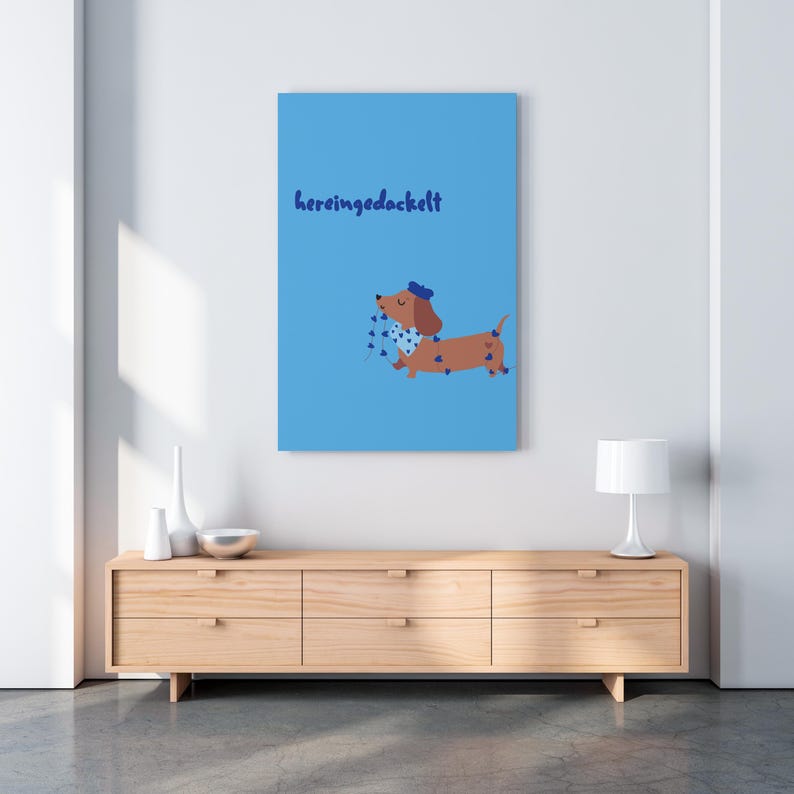K&ouml;nnte beinhalten: Blauer Leinwanddruck mit einem Cartoon-Dackel, der einen blauen Hut und einen Schal mit blauen Herzen tr&auml;gt. Der Druck hat das Wort "hereingedackelt" in blauer Schrift. Der Dackel ist braun mit blauen Herzakzenten.