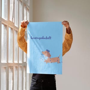 K&ouml;nnte beinhalten: Ein hellblaues Poster mit dem Text "hereingedackelt" in Dunkelblau. Das Poster zeigt einen Cartoon-Dackel mit blauem Hut und blauer Fliege, mit blauen herzf&ouml;rmigen Akzenten.