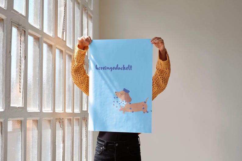 K&ouml;nnte beinhalten: Ein hellblaues Poster mit dem Text "hereingedackelt" in Dunkelblau. Das Poster zeigt einen Cartoon-Dackel mit blauem Hut und blauer Fliege, mit blauen herzf&ouml;rmigen Akzenten.