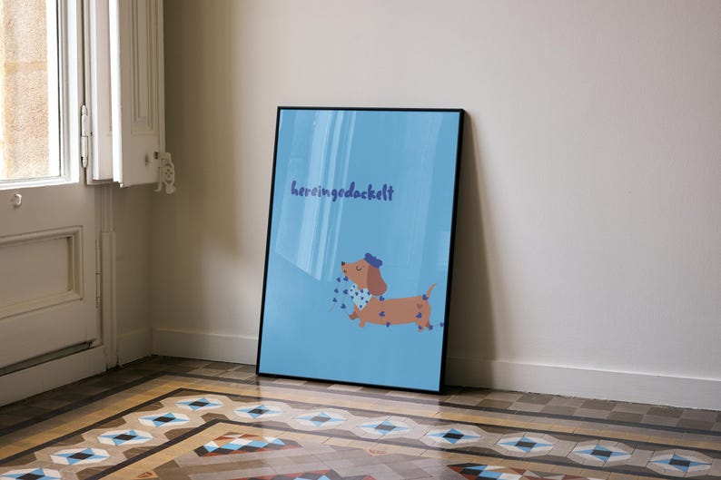 K&ouml;nnte beinhalten: Gerahmter Kunstdruck mit einem Cartoon-Dackel mit blauer Schleife und gepunktetem Schal auf hellblauem Hintergrund. Der Druck zeigt das Wort "heringgedackelt" in Schreibschrift.