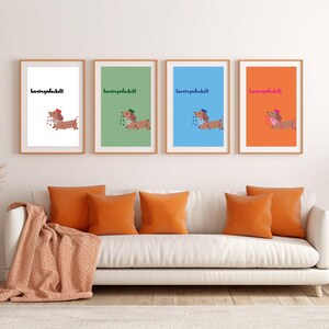 K&ouml;nnte beinhalten: Vier gerahmte Kunstdrucke mit Dackel-Illustrationen und dem Text "herzensdackel". Sie h&auml;ngen &uuml;ber einem wei&szlig;en Sofa mit orangefarbenen Kissen und einer Decke. Links befindet sich ein Beistelltisch mit Dekoration.