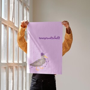 K&ouml;nnte beinhalten: Eine Person h&auml;lt ein lavendelfarbenes Poster mit dem Wort "rausgewatschelt" in lila Schrift hoch. Das Poster zeigt eine Cartoon-Ente mit Hut und Lichterkette. Die Person tr&auml;gt einen gelben Strickpullover.