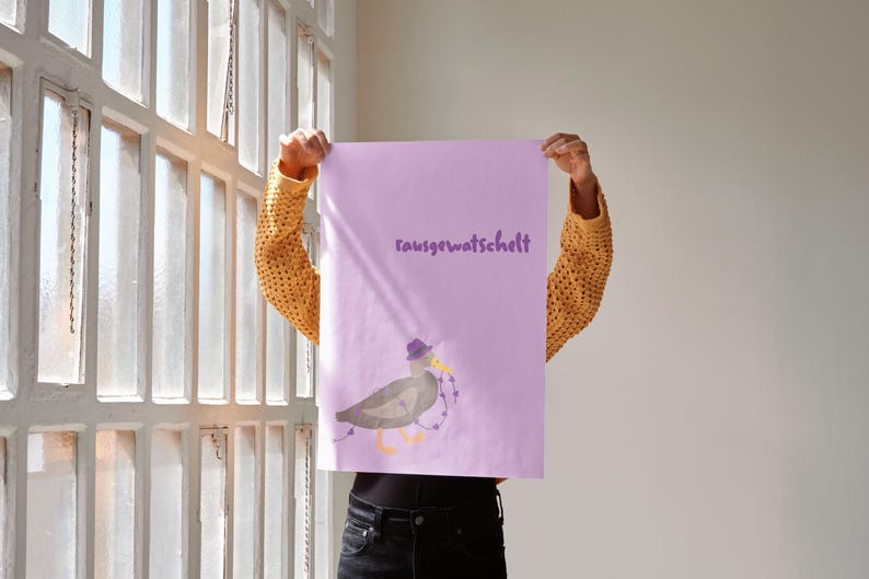 K&ouml;nnte beinhalten: Eine Person h&auml;lt ein lavendelfarbenes Poster mit dem Wort "rausgewatschelt" in lila Schrift hoch. Das Poster zeigt eine Cartoon-Ente mit Hut und Lichterkette. Die Person tr&auml;gt einen gelben Strickpullover.