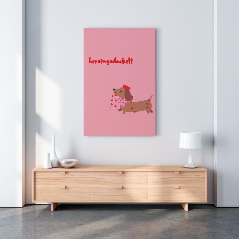 May include: A pink canvas print featuring a cartoon dachshund with a red bow and a scarf adorned with heart shapes. The dachshund is carrying a string of hearts. The text "hereingedackelt" is written in red.