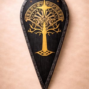 May include: A black wooden shield featuring a gold tree design and star accents. The shield has a pointed base and a metal trim with rivets. The tree design is centrally placed.