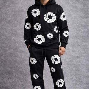 May include: Black hoodie and sweatpants set with a white floral pattern. The hoodie has a drawstring hood and a front pocket. The sweatpants have an elastic waistband and cuffs. The set is made of a soft material and is suitable for casual wear.