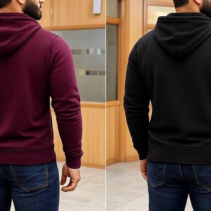 May include: Two hooded sweatshirts, one burgundy and one black, are displayed. Both have long sleeves and a drawstring hood. The sweatshirts are shown from the back, with the models wearing blue jeans. The background is a wooden paneled wall.
