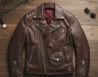 May include: A brown leather jacket with a classic biker style. The jacket features a notched collar, multiple zippered pockets, and a diagonal zipper closure. The jacket is hanging on a wooden hanger against a wooden background.