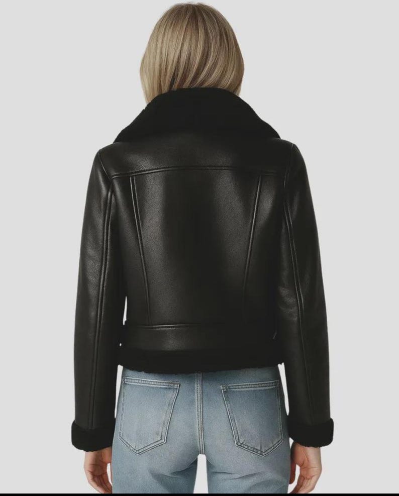 May include: Black faux leather jacket with a shearling collar and cuffs. The jacket features a classic aviator design with a belted waist and a zip closure. The jacket is shown from the back, with light blue jeans visible.