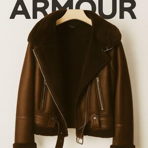 May include: Brown faux leather jacket with a shearling collar and lining. The jacket features a zipper closure, multiple pockets, and a belt detail. The text "SUPER ARMOUR" is displayed at the top.