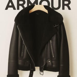 May include: Black leather jacket with a shearling collar and lining, featuring a diagonal zipper closure, belt, and the text "SUPER ARMOUR" in large black letters.