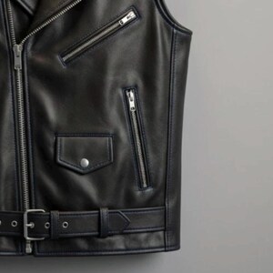 May include: Black leather vest with silver zippers, a small pocket with a snap closure, and a belt with a buckle. The vest has a classic biker style with a tailored fit. The vest is sleeveless.