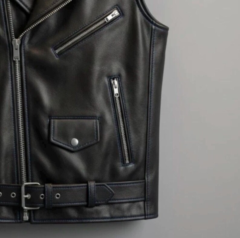 May include: Black leather vest with silver zippers, a small pocket with a snap closure, and a belt with a buckle. The vest has a classic biker style with a tailored fit. The vest is sleeveless.
