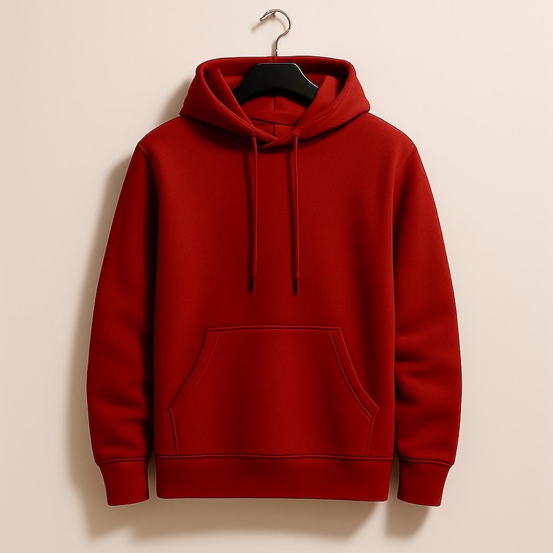 K&ouml;nnte beinhalten: Ein einfarbiger roter Kapuzenpullover mit Kordelzug und K&auml;ngurutasche. Der Pullover h&auml;ngt an einem schwarzen Kleiderb&uuml;gel vor einem neutralen Hintergrund. Der Hoodie ist aus weichem Material.
