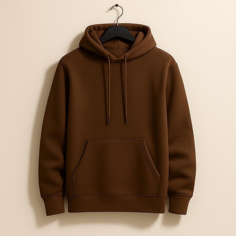 K&ouml;nnte beinhalten: Ein einfarbiger brauner Kapuzenpullover mit einer K&auml;ngurutasche und einer Kapuze mit Kordelzug. Der Pullover h&auml;ngt an einem schwarzen Kleiderb&uuml;gel. Der Stoff scheint ein weiches, mittelschweres Material zu sein.