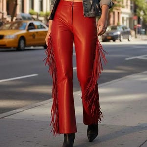 May include: Bright red leather pants with fringe detailing down the sides. The pants have a flared leg and are paired with black boots. The image is taken outdoors on a city street.