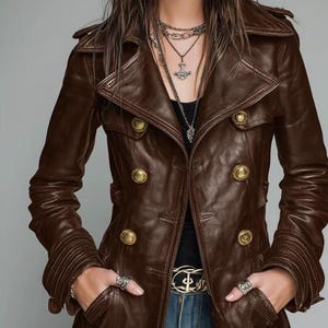 以下が含まれることがあります： ダブルブレストのデザインと金色のボタンが付いた茶色のレザージャケット。 ジャケットはノッチカラー、長袖、ポケット付きです。 モデルは黒いトップスとブルージーンズを着ています。
