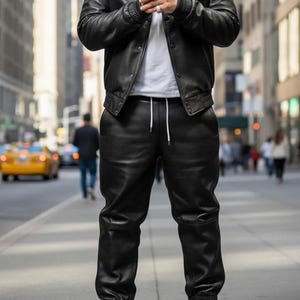 May include: A person wearing a black leather jacket and matching leather pants with white sneakers. The jacket has a collar and button closure. The pants have a drawstring waist and elastic cuffs. The background is a city street.