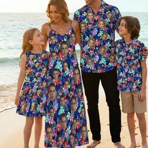 以下が含まれることがあります： ビーチで、お揃いの服を着た4人家族。服には、スパゲッティストラップのドレス、ボタンダウンシャツ、ノースリーブドレスがあり、すべて青い花柄と顔が描かれています。男の子はカーキ色のショートパンツを履いています。