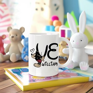 Pu&ograve; includere: Tazza in ceramica bianca con un design di Topolino, la parola "LOVE" e il nome "WILLIAM". La tazza &egrave; circondata da giocattoli, tra cui un coniglietto bianco e orsacchiotti. La tazza ha un manico.