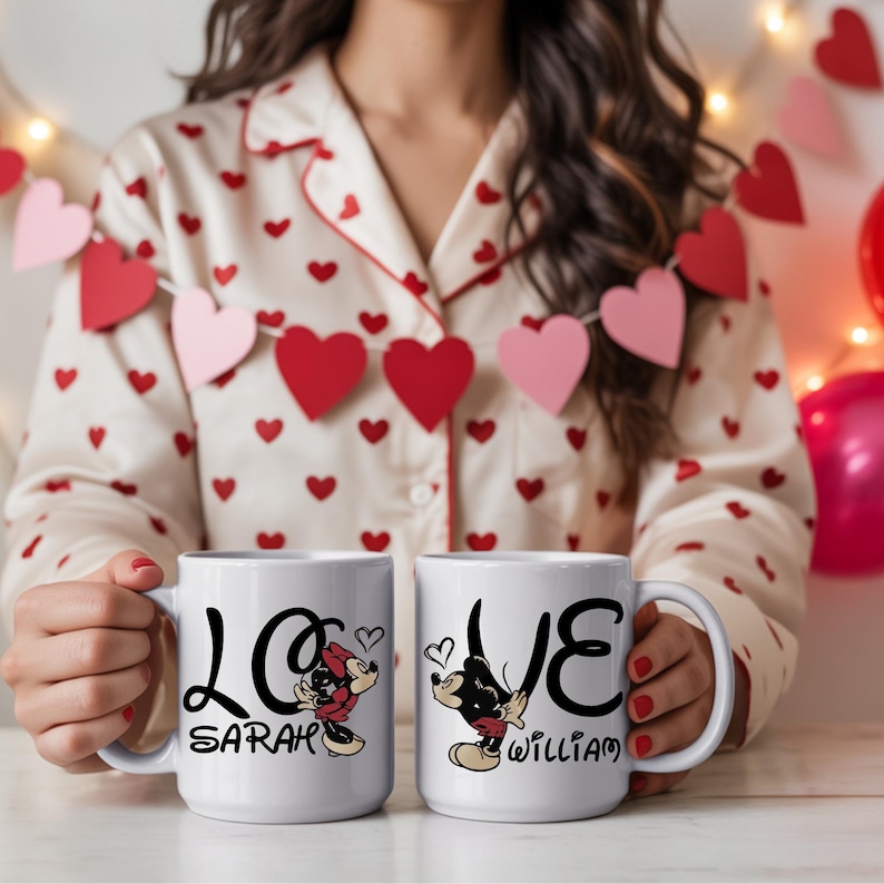Pu&ograve; includere: Due tazze in ceramica bianca con la parola "LOVE" in corsivo nero, con illustrazioni di Topolino e Minnie. Una tazza dice "Sarah" e l'altra dice "William". Le tazze sono tenute davanti a una persona che indossa un top di pigiama a forma di cuore.