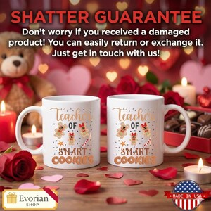 Pu&ograve; includere: Due tazze in ceramica bianca con la scritta "Teacher of Smart Cookies" in lettere dorate, con grafiche di omini di pan di zenzero. Le tazze sono su una superficie di legno con candele, petali di rosa e un adesivo "Made in USA".