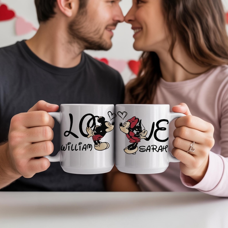 May include: Two white ceramic mugs with the word "LOVE" and Mickey and Minnie Mouse illustrations. One mug has "William" and the other has "Sarah" printed on it. The mugs are held by a couple.