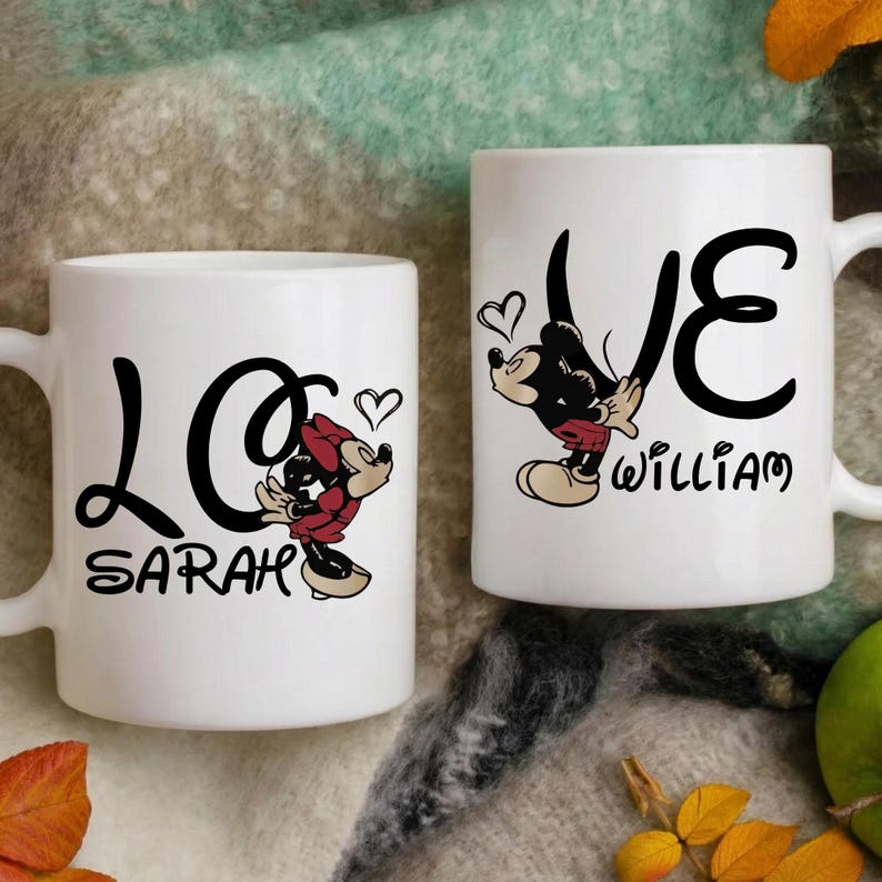 Pu&ograve; includere: Due tazze in ceramica bianca con scritte nere e disegni di personaggi dei cartoni animati. Una tazza dice "LOVE SARAH" con una grafica di Minnie Mouse, e l'altra dice "LOVE WILLIAM" con una grafica di Mickey Mouse. Entrambe le tazze hanno accenti a cuore.