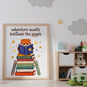 May include: A framed wall art print featuring a red panda reading a blue book atop a stack of colorful books. The text "adventure awaits between the pages" is printed above the red panda, surrounded by yellow stars on a white background.