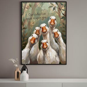 May include: A framed oil painting print featuring six white geese with orange beaks looking forward against a forest background. The text "Our collective gaze is upon you..." is written in dark grey script in the upper left corner of the artwork.
