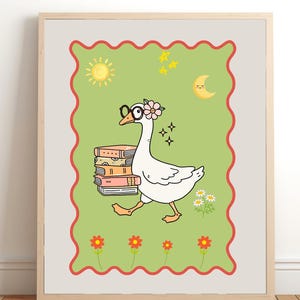 May include: A framed wall art print featuring a white goose wearing glasses and a pink flower on its head, carrying a stack of books. The background is light green with a red scalloped border, decorated with a yellow sun, moon, stars, and flowers.