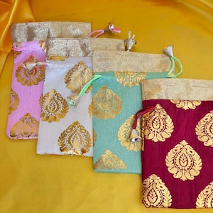 May include: A collection of small drawstring bags in various colors, including pink, white, teal, and burgundy. Each bag features a gold floral pattern and a gold-colored top. The bags are arranged on a yellow fabric background.
