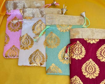 May include: A collection of small drawstring bags in various colors, including pink, white, teal, and burgundy. Each bag features a gold floral pattern and a gold-colored top. The bags are arranged on a yellow fabric background.