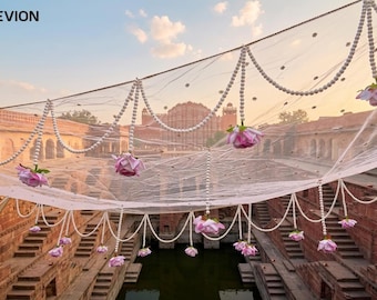 May include: A white sheer fabric canopy decorated with hanging strings of white pearls and artificial pink roses. The KAEVION brand name is printed in the top left corner. The decorative netting is draped horizontally across the frame.